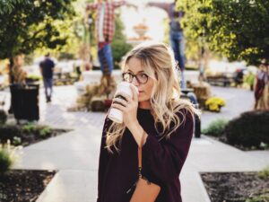 A woman with glasses sips coffee in a park
